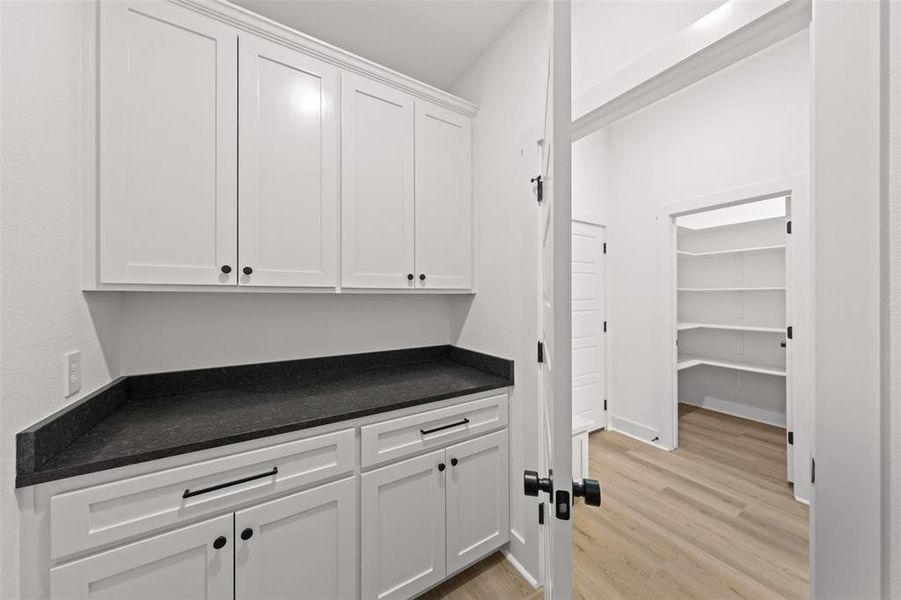 Bar featuring white cabinets, light wood-type flooring, and dark stone counters