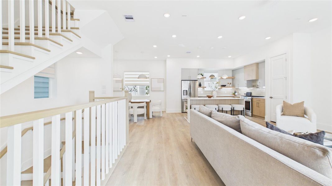 This open-concept living space features a modern kitchen with stainless steel appliances, a cozy living area with a neutral color palette, and stylish wood flooring. The bright, airy atmosphere is enhanced by recessed lighting and a sleek staircase leading to the upper level.