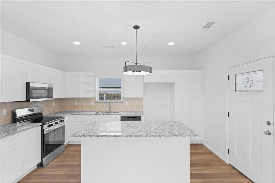 Modern kitchen featuring granite countertops, white shaker cabinetry, stainless steel appliances, and tile backsplash. Large center island provides ample prep space and additional seating.