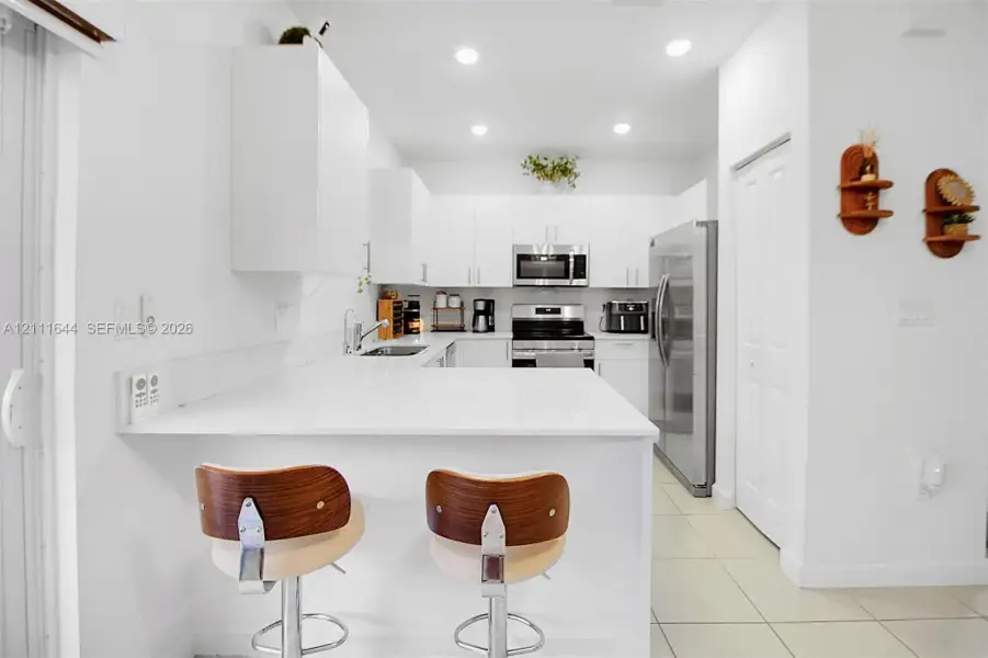Kitchen featuring white cabinetry, solid-surface countertops with a breakfast bar, recessed ceiling lighting, and stainless-steel appliances Kitchen featuring white cabinetry, solid-surface countertops with a breakfast bar, recessed ceiling lighting, and stainless-steel appliances