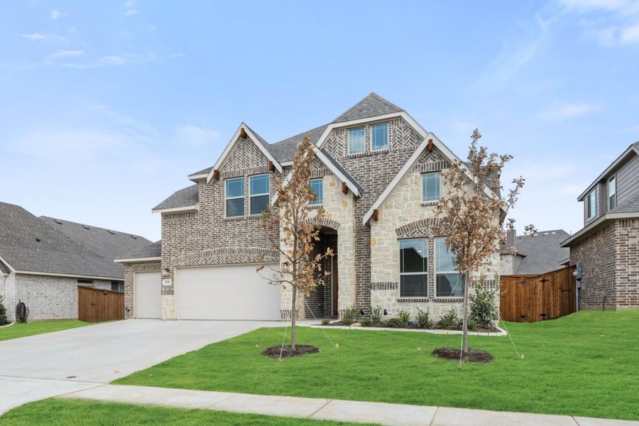 Two-story home with brick and stone exterior, two-car garage, and manicured front lawn with young trees