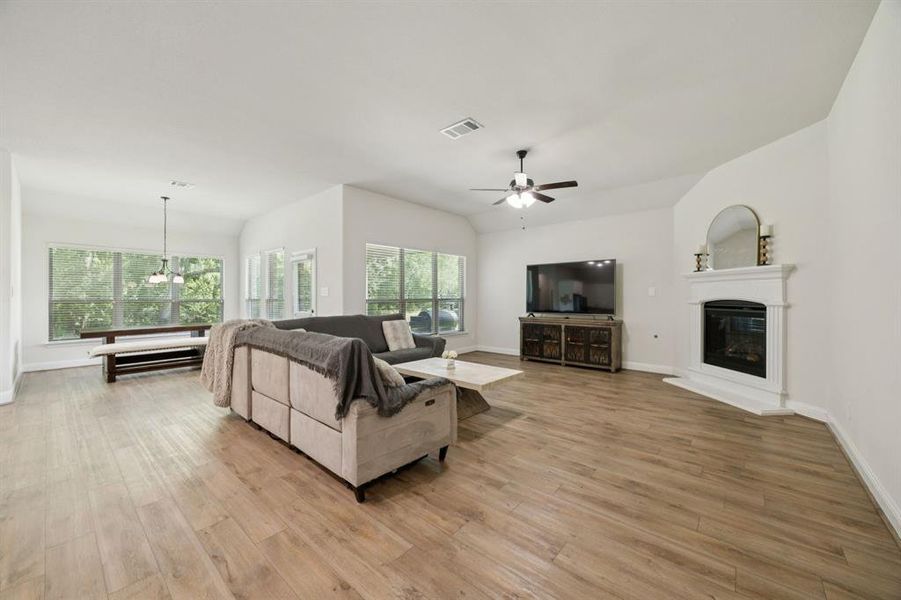Open concept living room with luxury vinyl plank flooring, ceiling fan, and a gas fireplace.