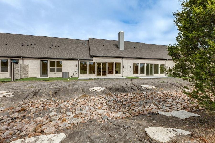 Back of house with a chimney, brick siding, central AC unit, and roof with shingles