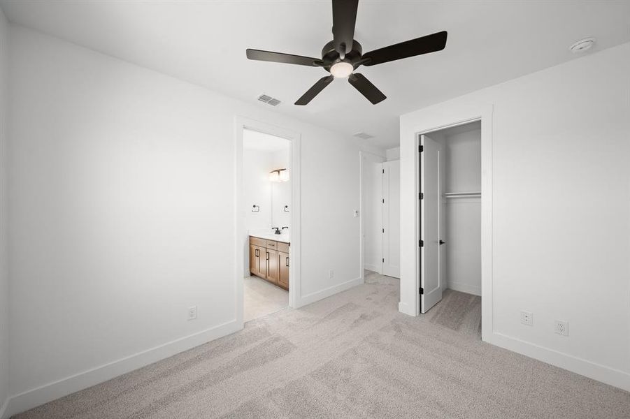 Unfurnished bedroom with a spacious closet, light carpet, ensuite bath, and a ceiling fan