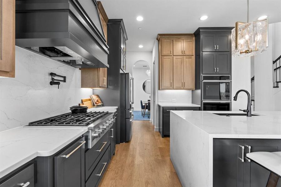 Kitchen featuring light stone countertops, premium range hood, light wood-style flooring, stainless steel gas cooktop, and pendant lighting Kitchen featuring light stone countertops, premium range hood, light wood-style flooring, stainless steel gas cooktop, and pendant lighting