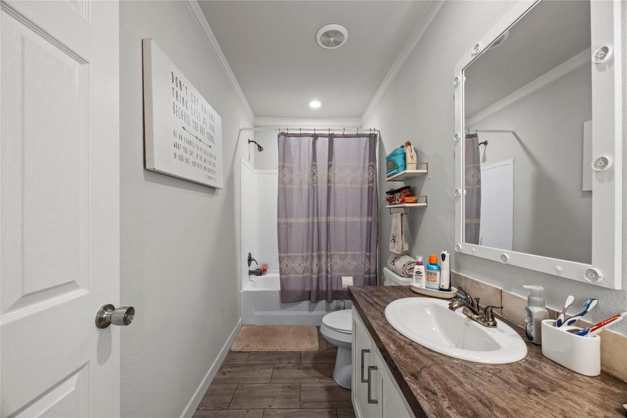 Bathroom featuring shower / tub combo with curtain, ornamental molding, vanity, and wood tiled floors