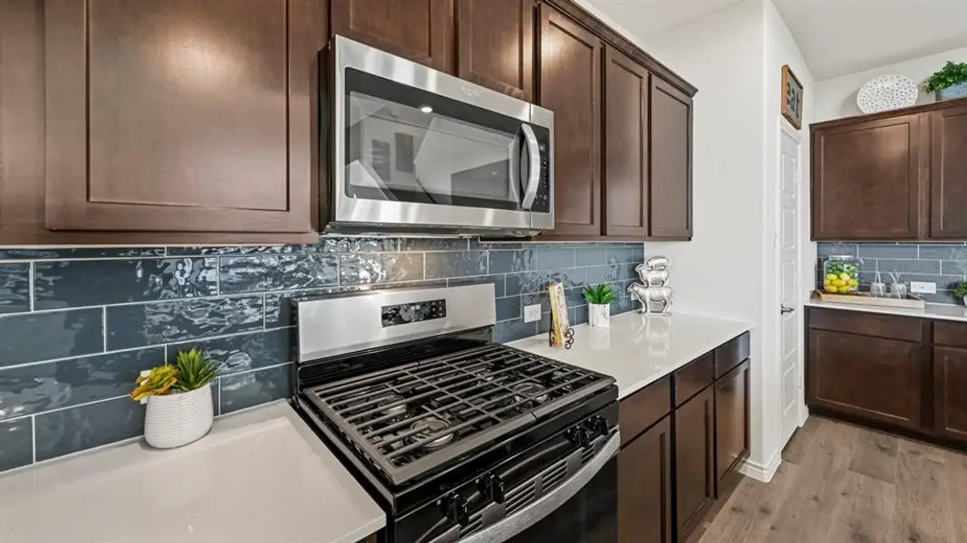 Kitchen featuring dark wood cabinetry, white countertops, a gas range with a stainless steel microwave, and blue subway tile backsplash