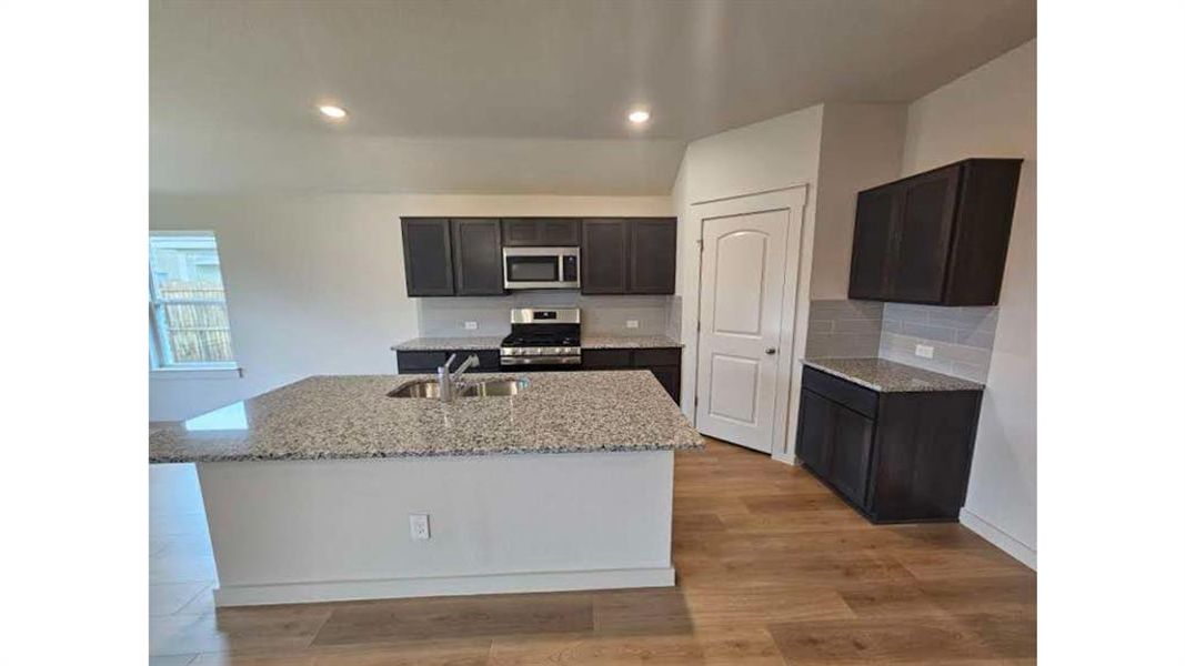 Kitchen featuring an island with a stainless steel sink, granite countertops, and dark wood cabinetry Kitchen featuring an island with a stainless steel sink, granite countertops, and dark wood cabinetry