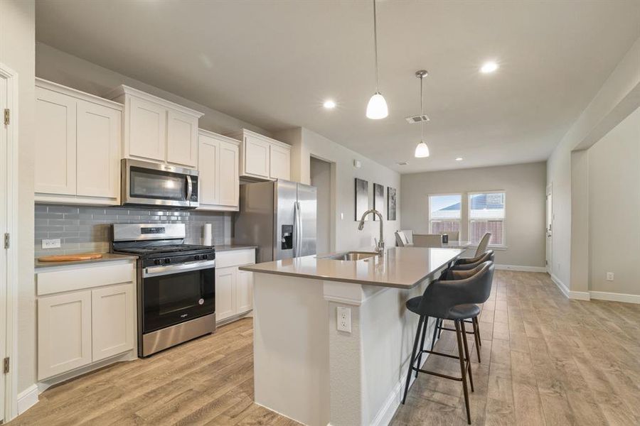 Kitchen with stainless steel appliances, a kitchen bar, a kitchen island with sink, tasteful backsplash, and light wood finished floors Kitchen with stainless steel appliances, a kitchen bar, a kitchen island with sink, tasteful backsplash, and light wood finished floors