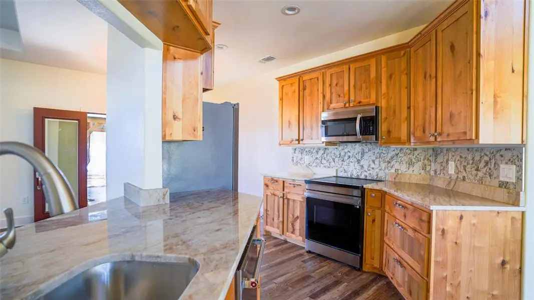 Kitchen featuring stainless steel appliances, light stone countertops, wood custom cabinetry, induction stovetop, and tasteful backsplash Kitchen featuring stainless steel appliances, light stone countertops, wood custom cabinetry, induction stovetop, and tasteful backsplash