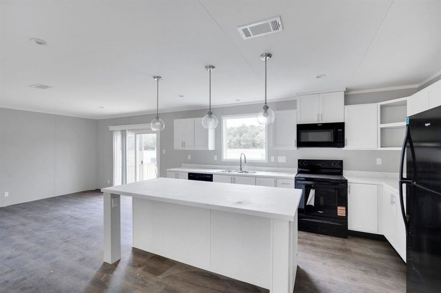 Open-concept kitchen featuring an island with a light-colored countertop, white cabinetry, dark appliances, wood-finish flooring, and pendant lighting