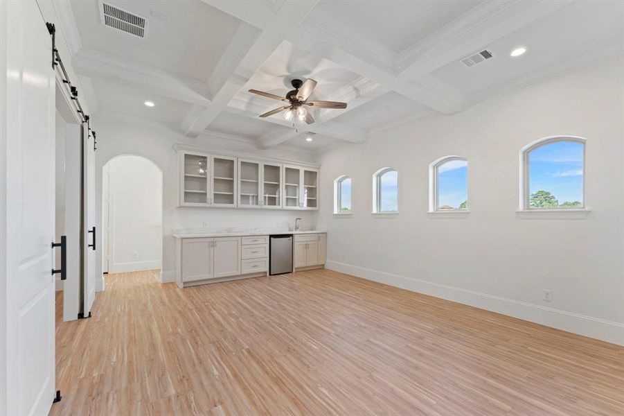 This is a spacious, bright  game room featuring hardwood floors, white built-in cabinetry with shelving, an elegant ceiling fan, recessed lighting, mini-fridge and charming arched windows that offer plenty of natural light.