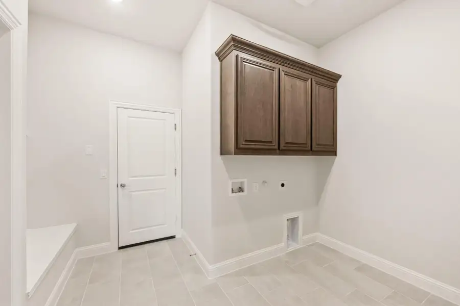 Laundry room with dark wood upper cabinets, washer and dryer hookups, and light tile flooring