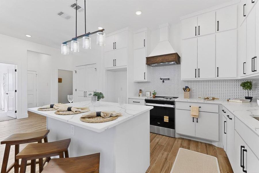 Kitchen featuring light stone counters, wood tiled floors, stainless steel range with electric cooktop, a center island, and decorative backsplash