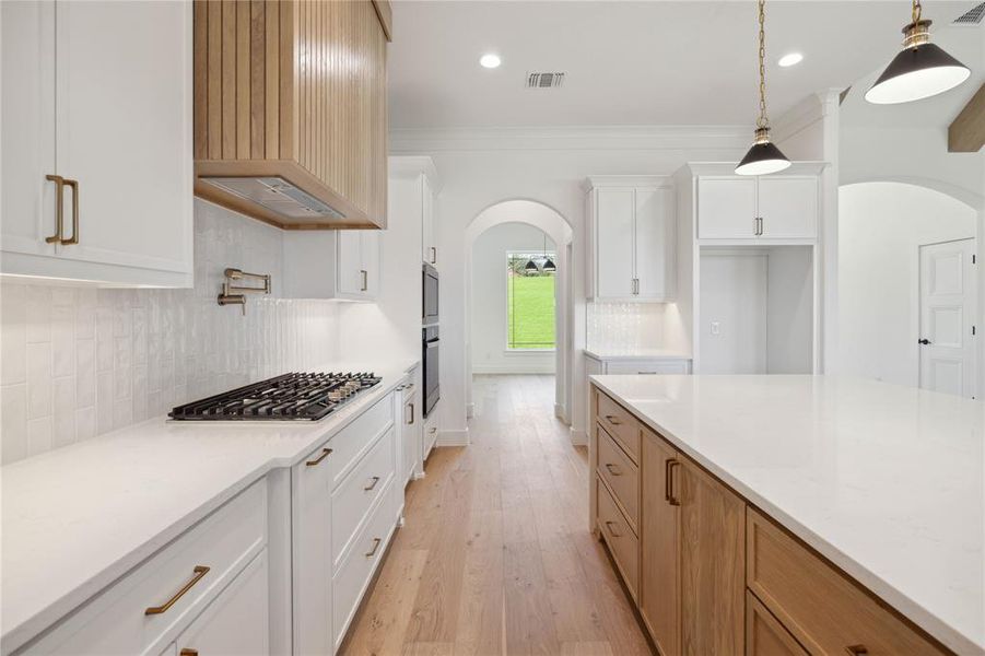 Kitchen with stainless steel appliances, hanging light fixtures, white cabinetry, light hardwood / wood-style flooring, and premium range hood