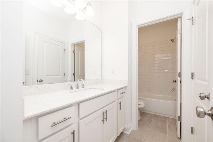 The shared hall bath has white cabinets, undermount sink and venetian marble countertop along with a steel tub/shower with tiles surround.