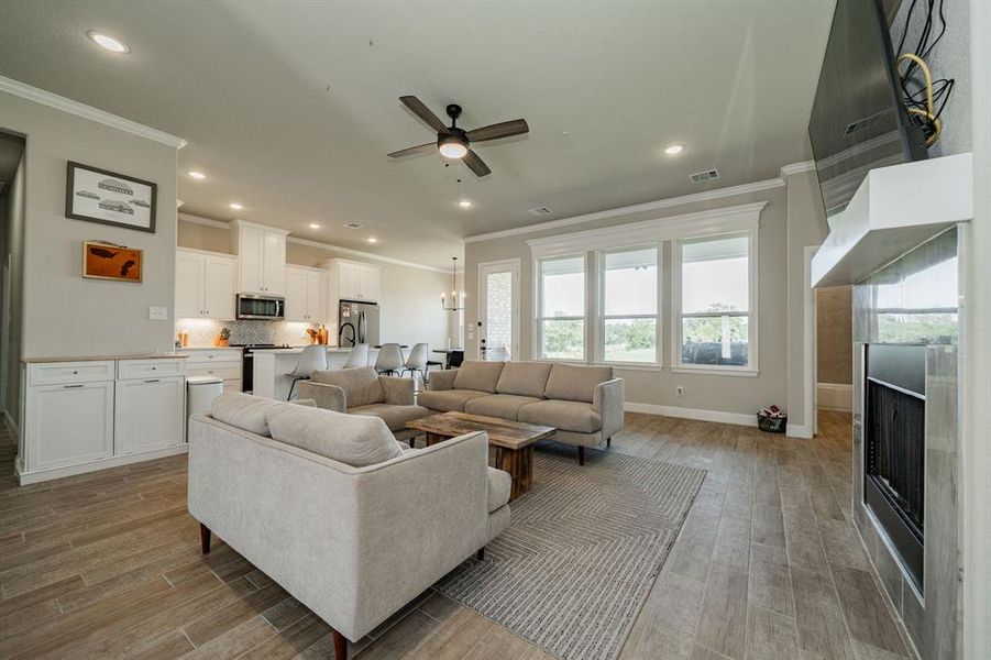 Living area with a fireplace, ornamental molding, light wood-type flooring, ceiling fan, and a chandelier Living area with a fireplace, ornamental molding, light wood-type flooring, ceiling fan, and a chandelier