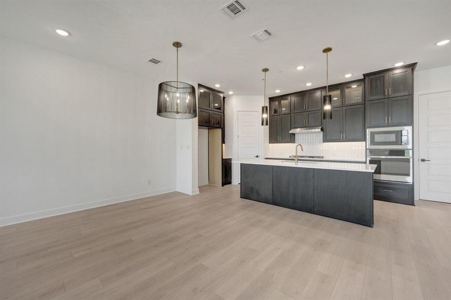 Modern kitchen featuring an island with a white countertop, dark cabinetry, and integrated stainless steel appliances Modern kitchen featuring an island with a white countertop, dark cabinetry, and integrated stainless steel appliances