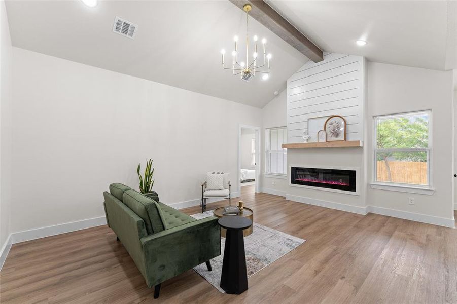 Living area featuring a chandelier, light wood-style flooring, baseboards, and a glass covered fireplace Living area featuring a chandelier, light wood-style flooring, baseboards, and a glass covered fireplace