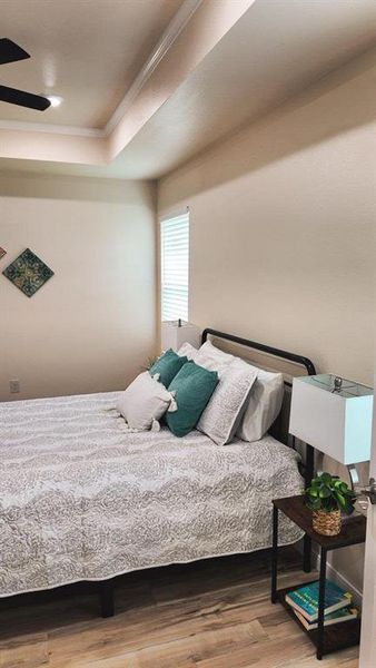 Recessed ceiling with crown molding, wood-finish flooring, ceiling fan with integrated lighting, and a single window with blinds