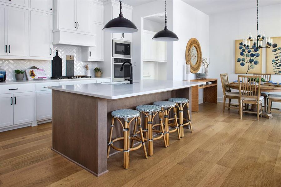 Kitchen featuring white cabinetry, decorative backsplash, pendant lighting, a kitchen bar, and a chandelier