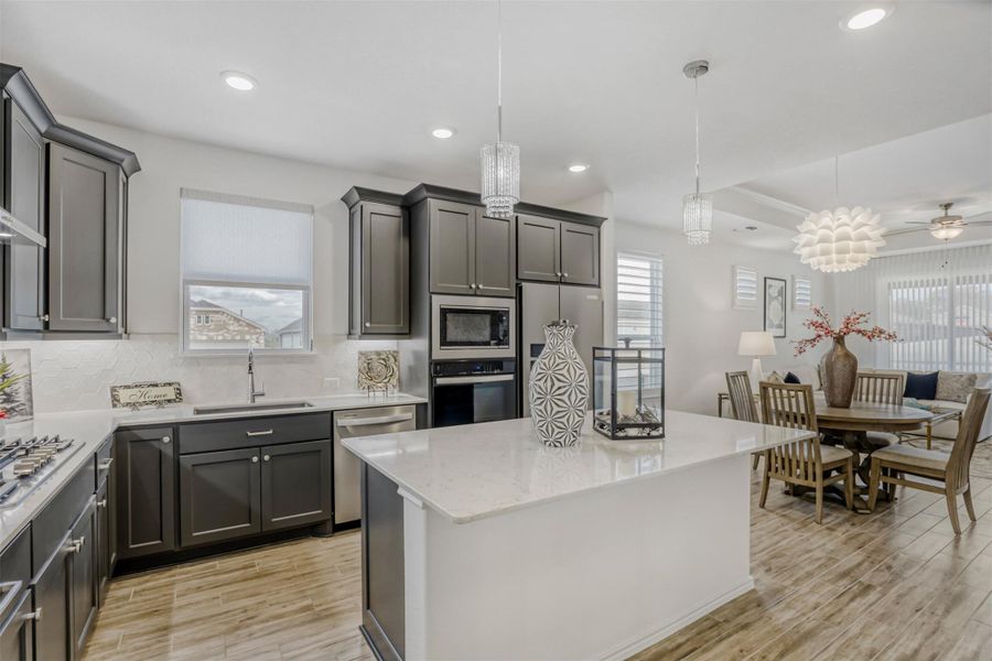 Kitchen with pendant and canned lighting, decorative backsplash, light wood-style floors, light stone countertops, and stainless steel appliances
