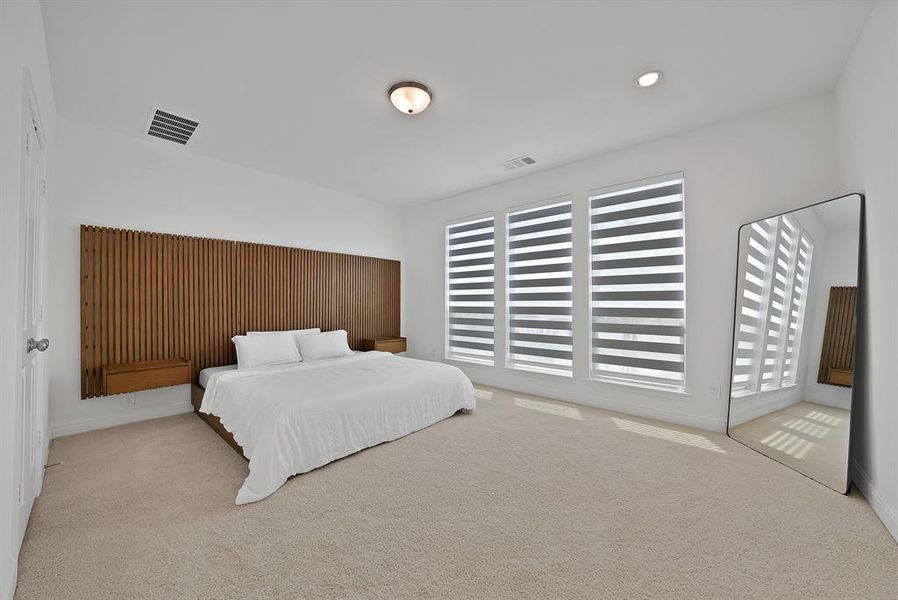 Expansive bedroom featuring a full-wall wood panel accent, three large windows with integrated blinds, and plush carpet flooring