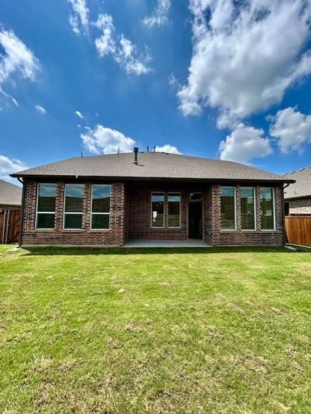 Expansive backyard featuring a green lawn, a brick exterior, a covered patio, and multiple large windows