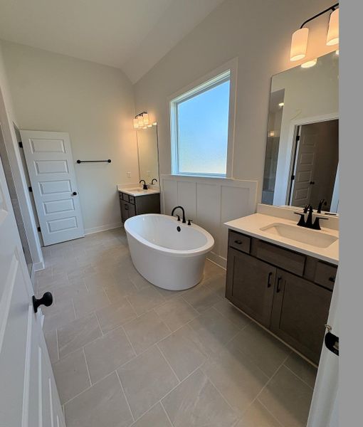 Spacious bathroom featuring a freestanding soaking tub, dual vanities with integrated sinks and quartz countertops, and large format tile flooring Spacious bathroom featuring a freestanding soaking tub, dual vanities with integrated sinks and quartz countertops, and large format tile flooring