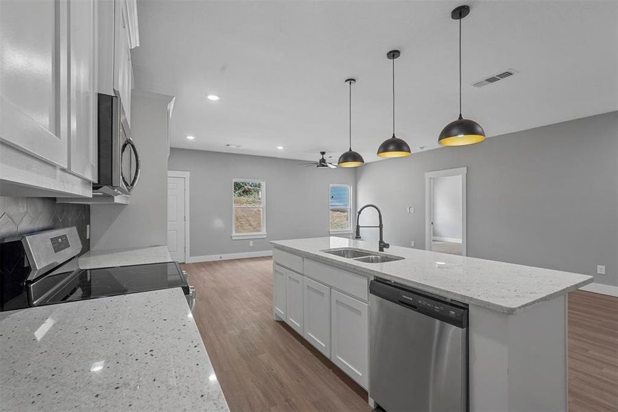 Kitchen with a kitchen island with sink, appliances with stainless steel finishes, white cabinetry, and sink