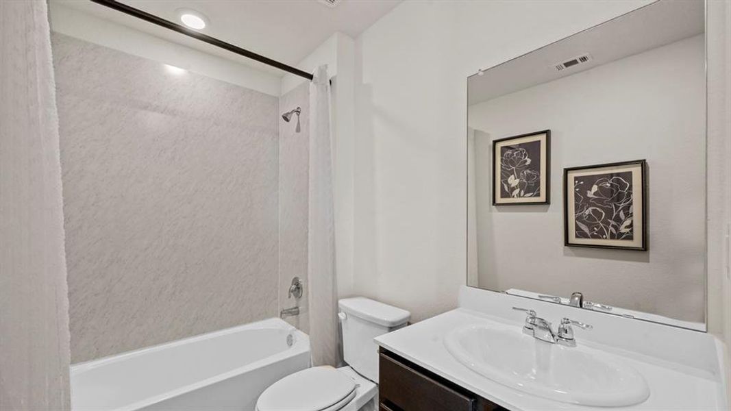 The bathroom features a bathtub with a shower, a vanity with an integrated sink, and a large mirror The bathroom features a bathtub with a shower, a vanity with an integrated sink, and a large mirror