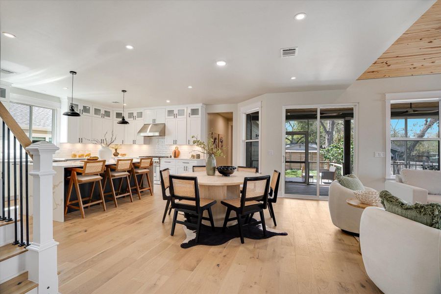 Open-concept living area featuring light wood flooring, a white kitchen with an island, and a dining area Open-concept living area featuring light wood flooring, a white kitchen with an island, and a dining area