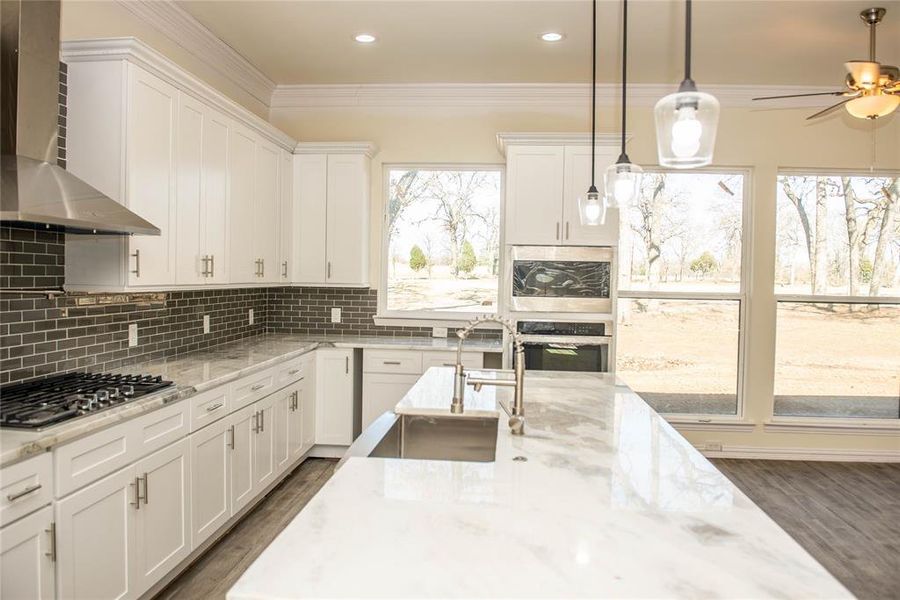 Kitchen featuring wall chimney range hood, white cabinetry, stainless steel appliances, tasteful backsplash, and ceiling fan