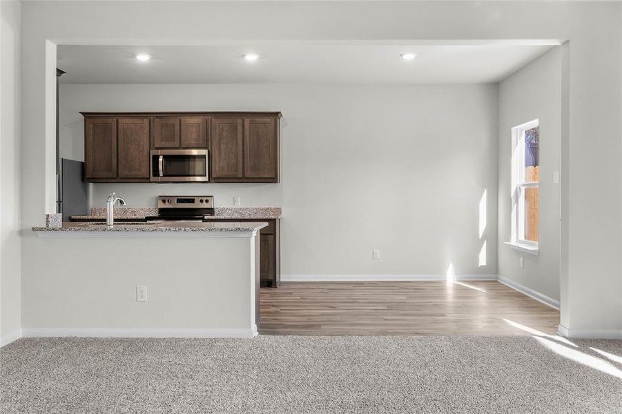 Kitchen with light stone counters, recessed lighting, a sink, dark brown cabinets, and appliances with stainless steel finishes