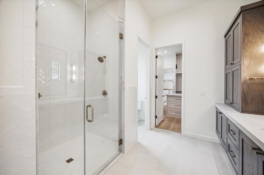 The glass-enclosed shower leads to a walk-in closet with custom built-ins for ample storage. Thoughtfully designed for comfort and convenience.