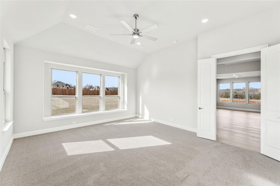 Empty bedroom with vaulted ceiling, ceiling fan, carpet flooring, and triple windows overlooking backyard Empty bedroom with vaulted ceiling, ceiling fan, carpet flooring, and triple windows overlooking backyard