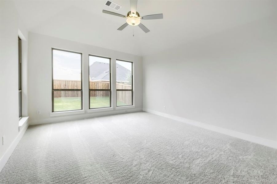 Spacious room featuring light-toned carpeting, three large windows, a fourth vertical window, and a ceiling fan with integrated lighting Spacious room featuring light-toned carpeting, three large windows, a fourth vertical window, and a ceiling fan with integrated lighting