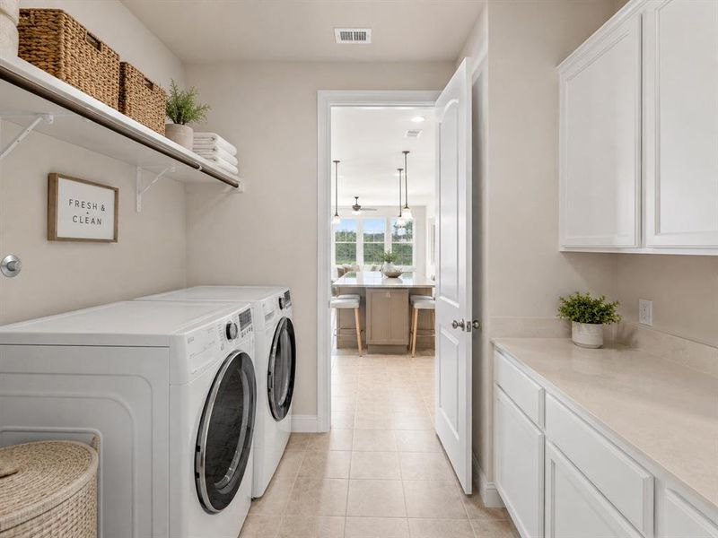 Dedicated laundry room featuring tile flooring, built-in shelving, white cabinetry, and an extended countertop