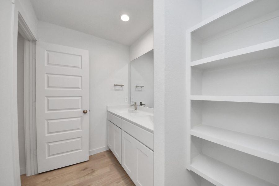 The second bathroom upstairs with white cabinetry, a large mirror, and open shelving. The space features wood-like flooring and a sleek, minimalist design.