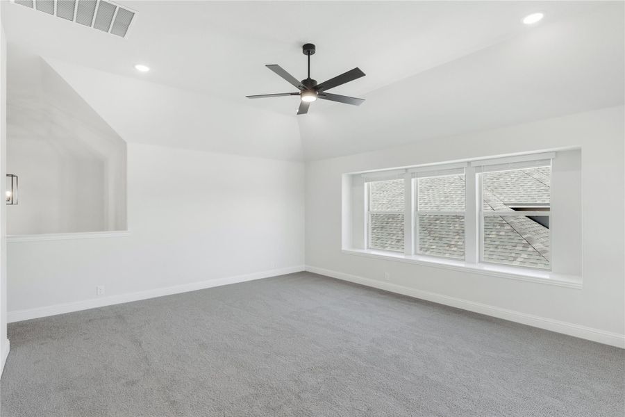 Empty bedroom with vaulted ceiling, ceiling fan, gray carpet, and large window Empty bedroom with vaulted ceiling, ceiling fan, gray carpet, and large window