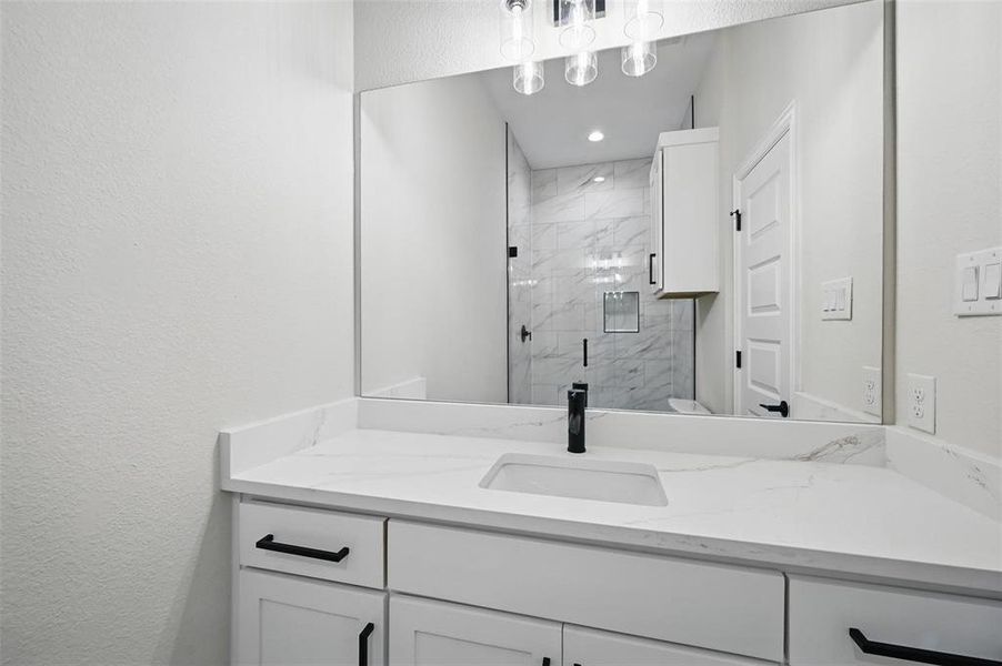 Full bathroom with a textured wall, vanity, and a marble finish shower Full bathroom with a textured wall, vanity, and a marble finish shower