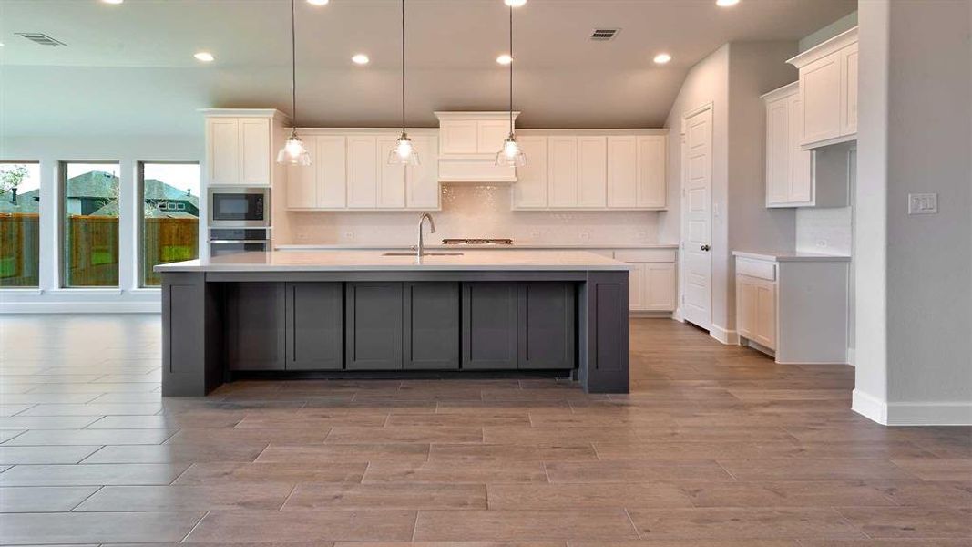 Kitchen with white cabinetry, a kitchen island with sink, black microwave, oven, and sink