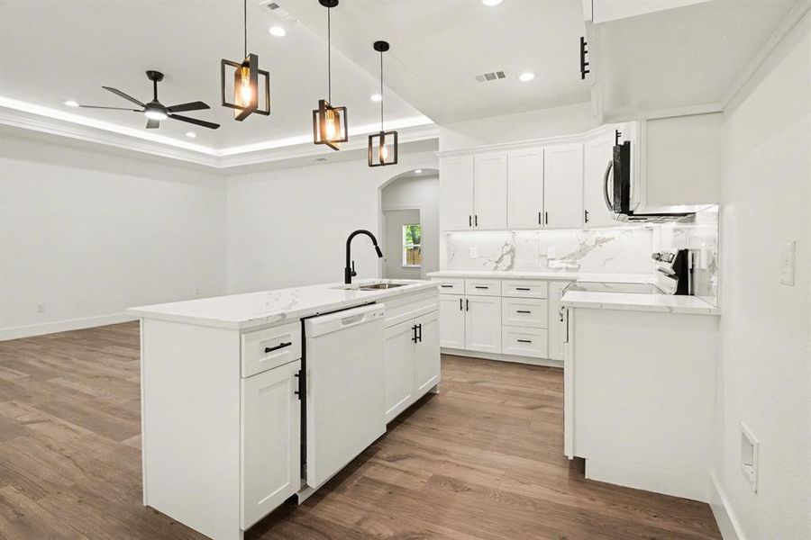 This kitchen features white cabinetry and countertops, a central island with a sink and dishwasher, and stylish pendant lighting