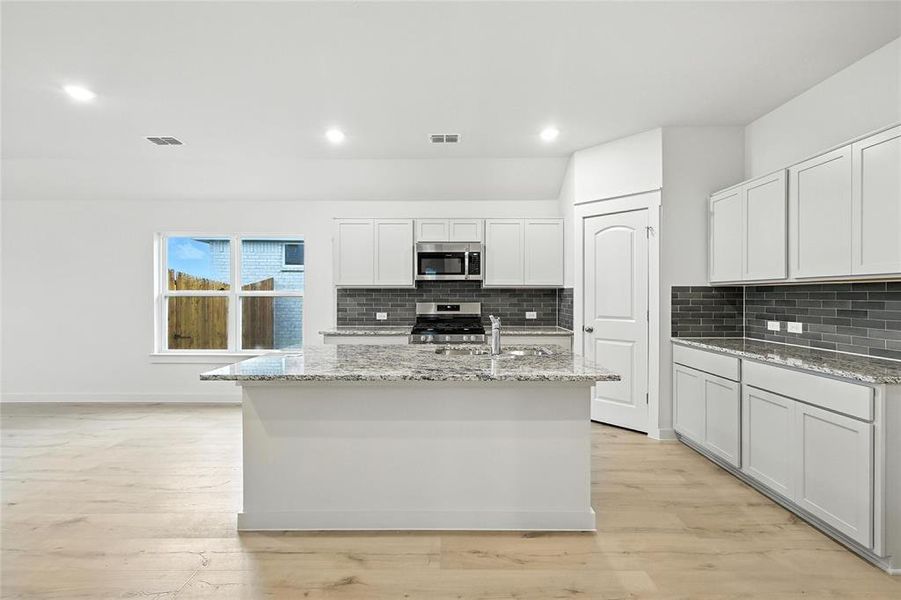 Kitchen with appliances with stainless steel finishes, a kitchen island with sink, tasteful backsplash, light stone countertops, and recessed lighting