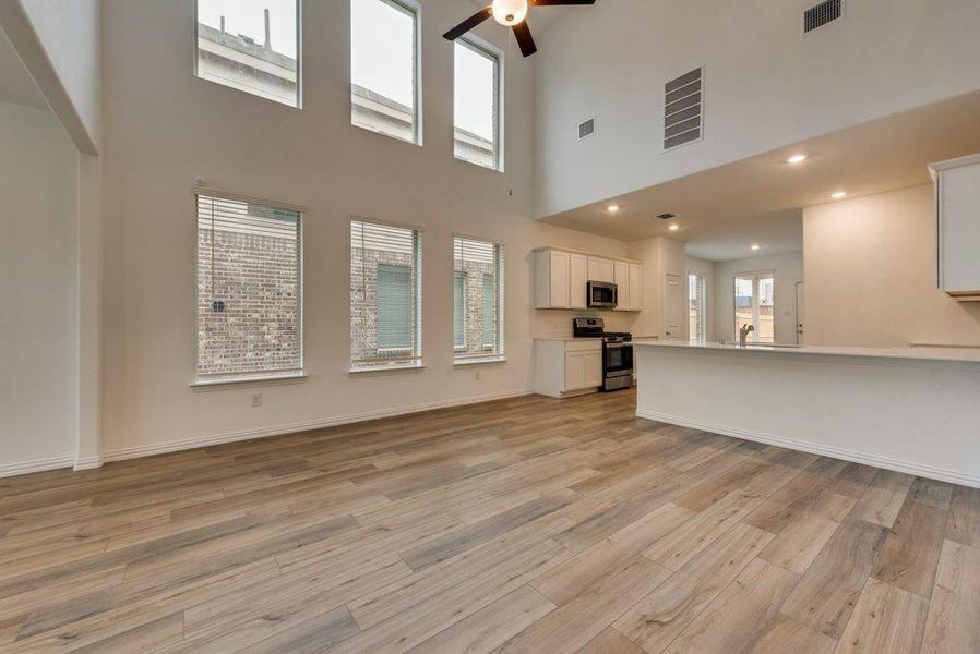 Unfurnished living room with ceiling fan, a high ceiling, and light hardwood / wood-style floors