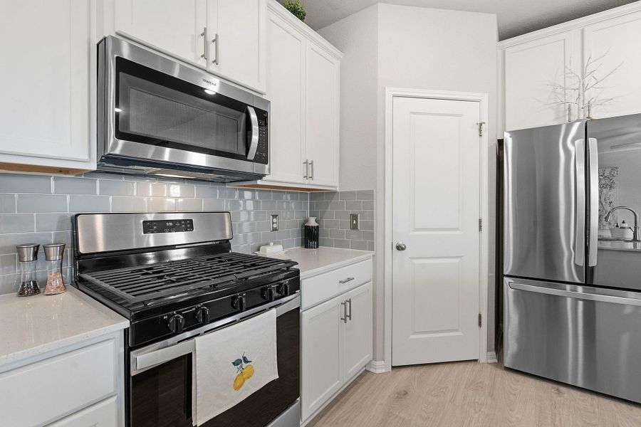 Kitchen featuring stainless steel appliances, white cabinetry, light wood-type flooring, tasteful backsplash, and light stone counters Kitchen featuring stainless steel appliances, white cabinetry, light wood-type flooring, tasteful backsplash, and light stone counters