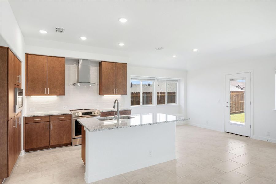 Kitchen with dark wood cabinets, granite island with sink, stainless steel range, and wall-mounted hood vent