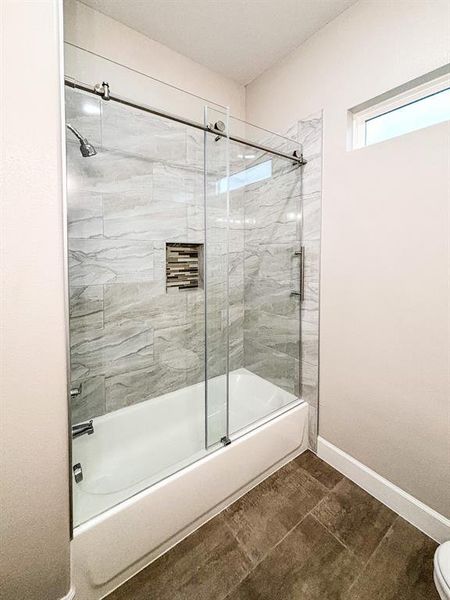 Bathroom with bath / shower combo with glass door and dark tile patterned floors Bathroom with bath / shower combo with glass door and dark tile patterned floors