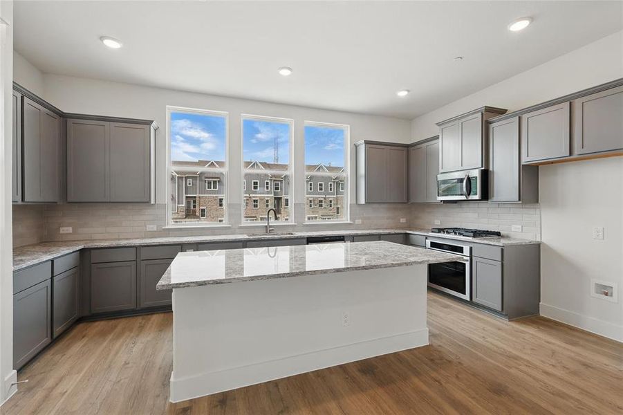 Kitchen with light stone counters, gray cabinets, stainless steel appliances, a kitchen island, and recessed lighting