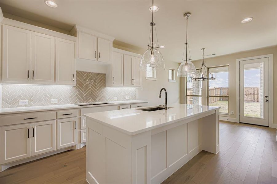 Kitchen featuring backsplash, pendant lighting, white cabinets, an island with sink, and light wood finished floors Kitchen featuring backsplash, pendant lighting, white cabinets, an island with sink, and light wood finished floors